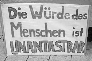 The image is a photograph of a large cardboard sign with the text Die Wrde des Menschen ist UNANTASTBAR.